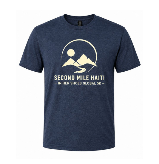 A navy blue heather crewneck t-shirt featuring a cream-colored graphic of mountains, a sun, and a winding road, with the text 'SECOND MILE HAITI - IN HER SHOES GLOBAL 5K -' printed below.