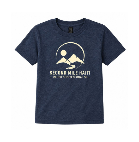A navy blue heathered short-sleeve t-shirt with a cream-colored graphic on the chest. The graphic features a minimalist mountain, sun, and winding road design inside a circle, with the text 'SECOND MILE HAITI - IN HER SHOES GLOBAL 5K -' printed below.
